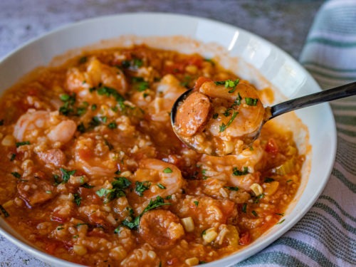 An inviting outdoor setting for a Jambalaya feast, with a large, communal cast-iron pot over an open flame, surrounded by guests eagerly awaiting to dig into the aromatic and savory blend of spices, meats, and rice.