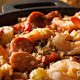 A steaming pot of Creole Jambalaya, rich with tomatoes, showcasing a colorful mix of shrimp, chicken, and andouille sausage, garnished with fresh green onions and served on a rustic wooden table.