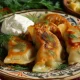 A vibrant, close-up image of a hand-crafted pierogi being filled with a rich, creamy mixture of mashed potato and cheese, highlighting the skillful process of folding and sealing the dough, with a bowl of filling and a dusted flour surface in the background.