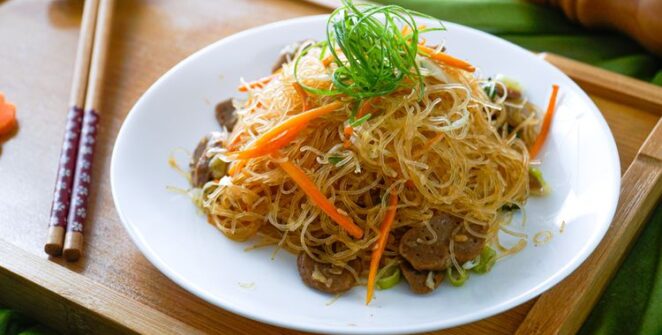 Sepiring bihun goreng klasik dengan tambahan sayuran segar dan potongan ayam, disajikan dengan taburan bawang goreng