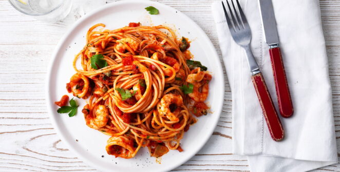 Sepiring spaghetti seafood dengan udang, cumi, dan kerang, disajikan dengan saus tomat yang kaya rasa dan aroma segar
