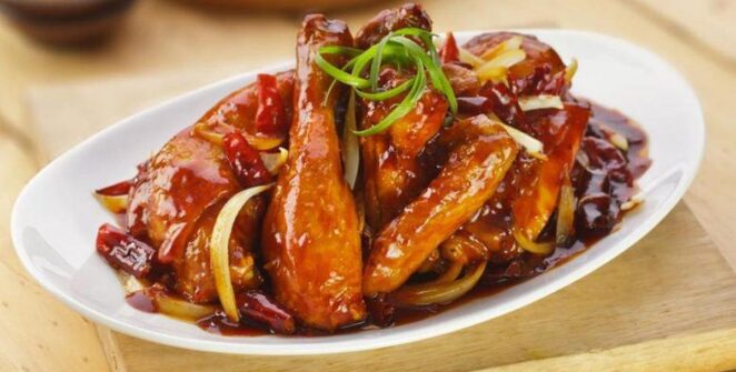 Ayam kecap manis dengan warna cokelat mengilap dan potongan daun bawang, tampak lezat dan menggugah selera