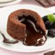 Lava cake cokelat dengan bagian luar yang lembut dan isi cokelat lumer di dalam, disajikan dengan es krim vanila dan buah segar