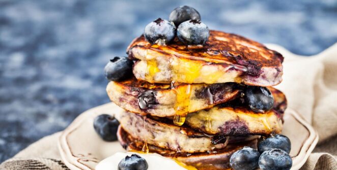 Tumpukan pancake blueberry fluffy lembut dengan siraman maple syrup dan blueberry segar