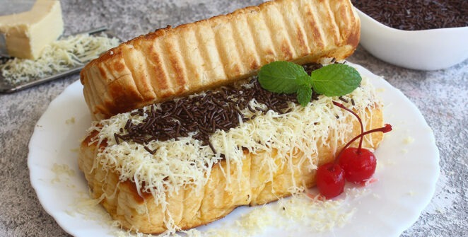 Sepiring roti bakar keemasan dengan topping cokelat leleh dan keju parut