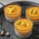 Puding mangga susu tersaji dalam gelas transparan, dihiasi dengan potongan mangga segar