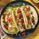 A colorful platter of Tacos Mexican Fiesta with marinated meats, fresh vegetables, and vibrant toppings